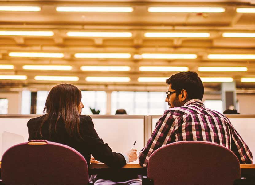 two people viewed from behind sitting at a desk and looking at each other