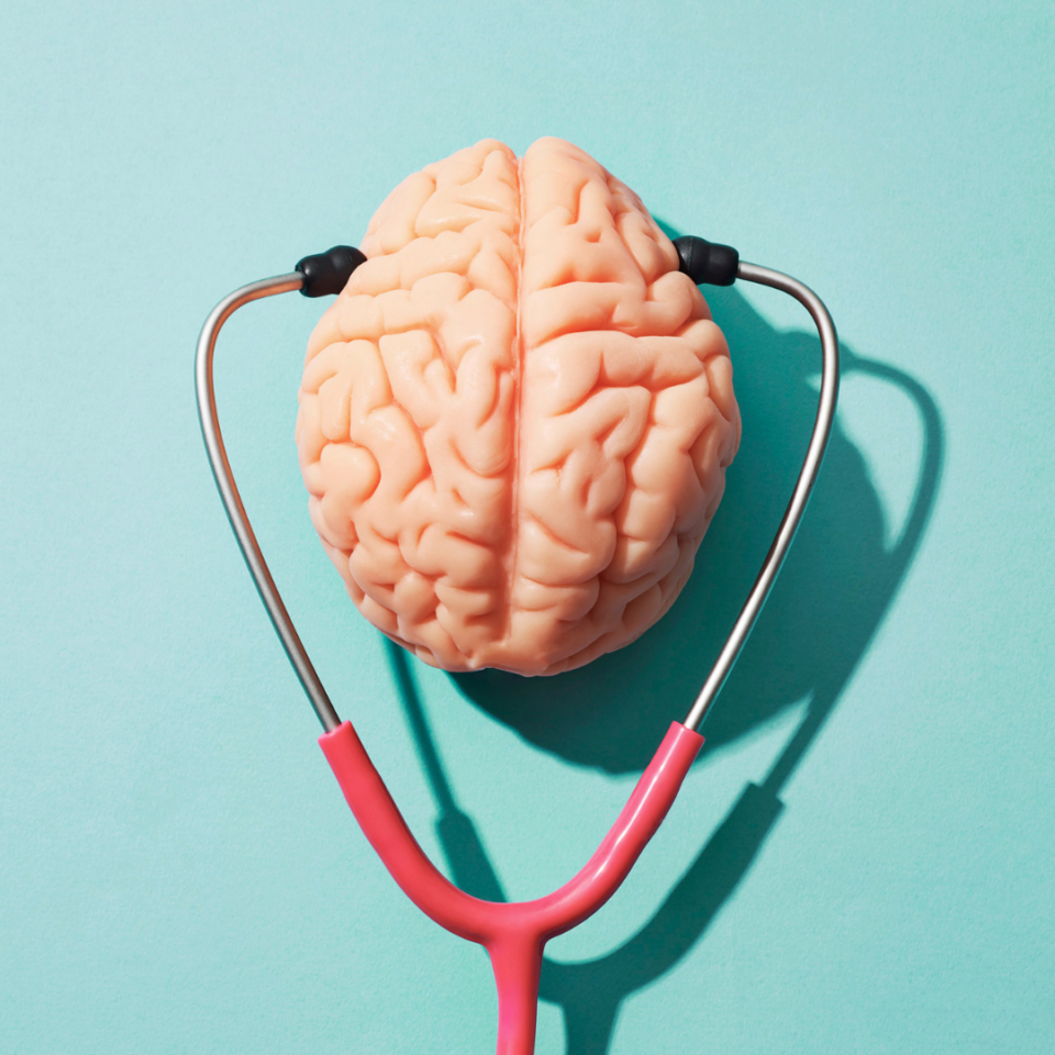 Image is a plastic brain seen from the top. A stethescope is placed on the brain as though the brain is wearing it. There is a light blue background.